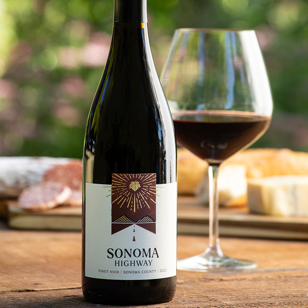 Photo of Sonoma Highway Pinot Noir bottle on a table with poured glass and cheese tray